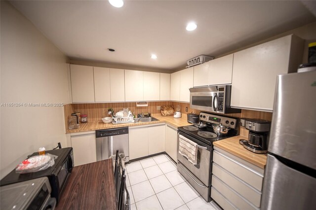 kitchen with tasteful backsplash, white cabinetry, sink, light tile patterned floors, and stainless steel appliances