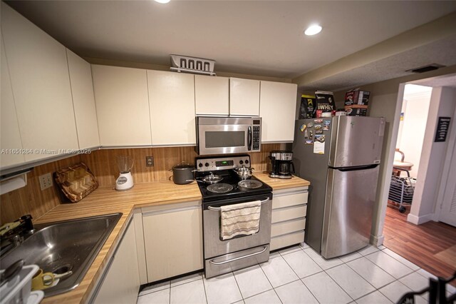 kitchen featuring appliances with stainless steel finishes, tasteful backsplash, sink, white cabinets, and light tile patterned floors