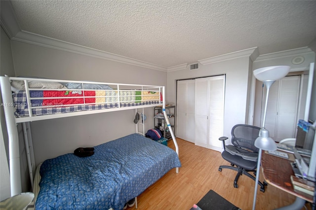 bedroom with a textured ceiling, wood finished floors, a closet, and ornamental molding