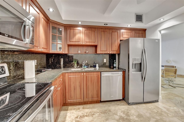 kitchen featuring dark stone countertops, backsplash, sink, a tray ceiling, and appliances with stainless steel finishes