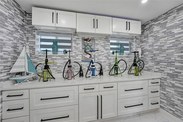 bar with backsplash, light stone counters, and white cabinetry