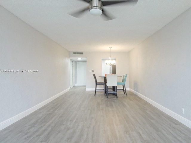 unfurnished dining area featuring ceiling fan with notable chandelier and light hardwood / wood-style floors