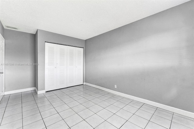 unfurnished bedroom featuring a textured ceiling, light tile patterned floors, and a closet