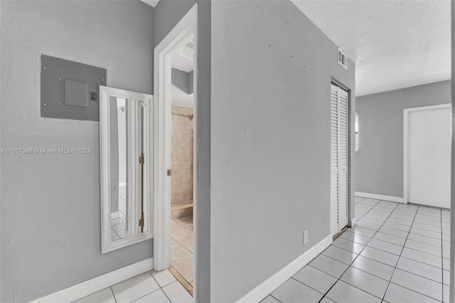 corridor with a textured ceiling, light tile patterned floors, and electric panel