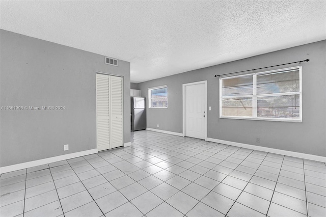 tiled empty room featuring a textured ceiling and a wealth of natural light