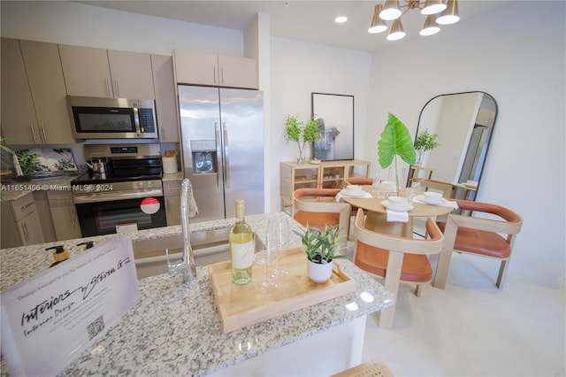 kitchen featuring appliances with stainless steel finishes, light stone countertops, an inviting chandelier, and sink