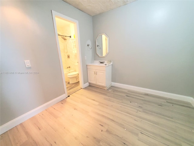 unfurnished bedroom featuring a textured ceiling, ensuite bath, sink, and light hardwood / wood-style floors