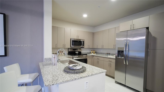 kitchen featuring stainless steel appliances, light stone counters, kitchen peninsula, sink, and a breakfast bar area