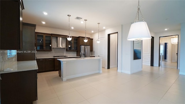 kitchen featuring wall chimney range hood, gas cooktop, a center island with sink, stainless steel fridge with ice dispenser, and tasteful backsplash