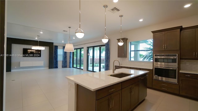 kitchen with a kitchen island with sink, sink, decorative backsplash, hanging light fixtures, and appliances with stainless steel finishes