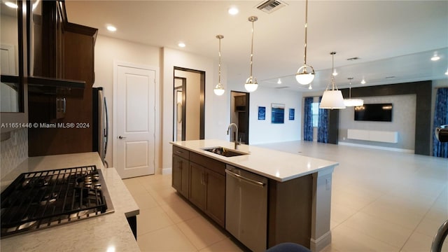 kitchen featuring dark brown cabinets, stainless steel appliances, decorative light fixtures, sink, and an island with sink