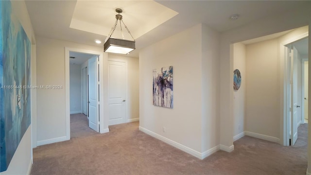 corridor featuring a raised ceiling and light carpet