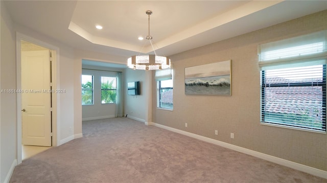 spare room featuring light carpet, a raised ceiling, and a notable chandelier