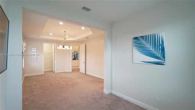 empty room with a tray ceiling, a chandelier, and light carpet