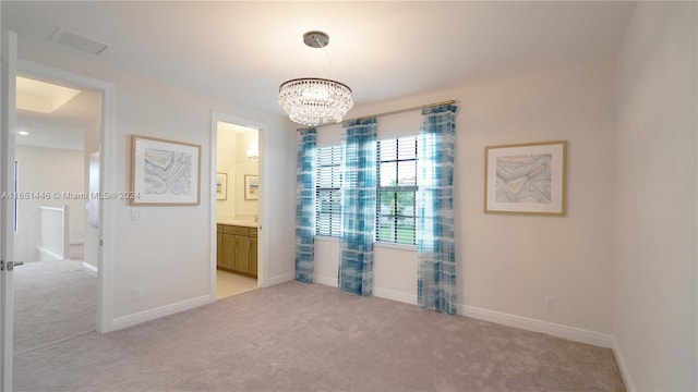 spare room featuring a chandelier and light colored carpet