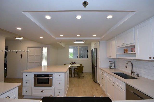 kitchen with a tray ceiling, recessed lighting, appliances with stainless steel finishes, white cabinetry, and a sink