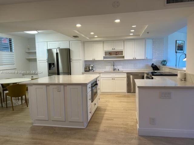 kitchen with kitchen peninsula, sink, appliances with stainless steel finishes, white cabinets, and light hardwood / wood-style floors