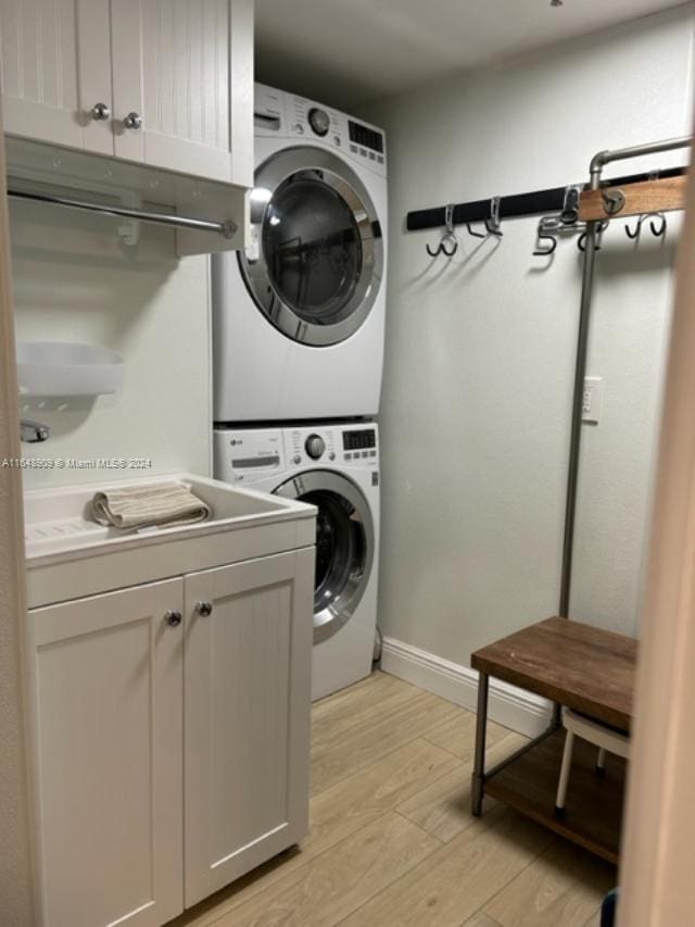 washroom featuring stacked washing maching and dryer, cabinets, and light wood-type flooring