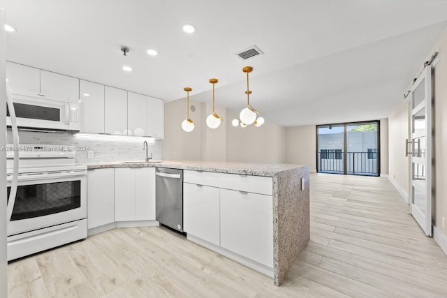 kitchen with decorative light fixtures, white appliances, a barn door, and white cabinets