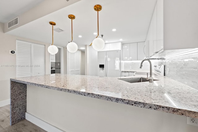 kitchen with hanging light fixtures, decorative backsplash, light wood-type flooring, white fridge with ice dispenser, and sink