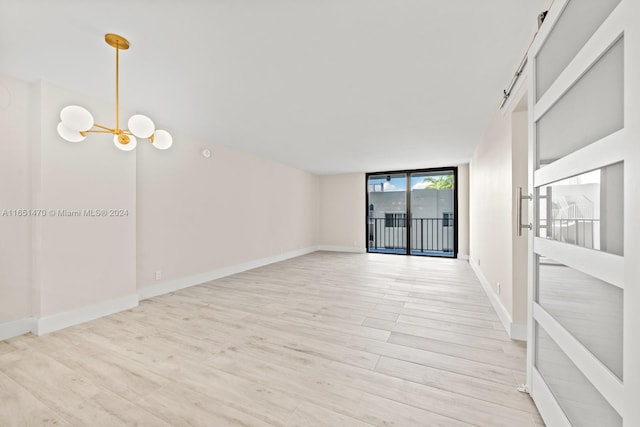 spare room with an inviting chandelier, light wood-type flooring, and expansive windows