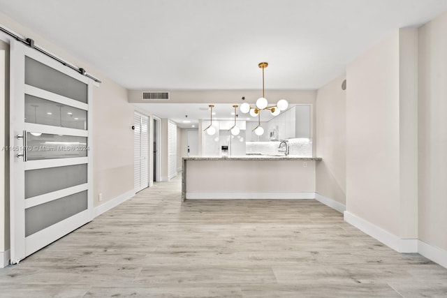 unfurnished dining area featuring light hardwood / wood-style flooring, a notable chandelier, and a barn door