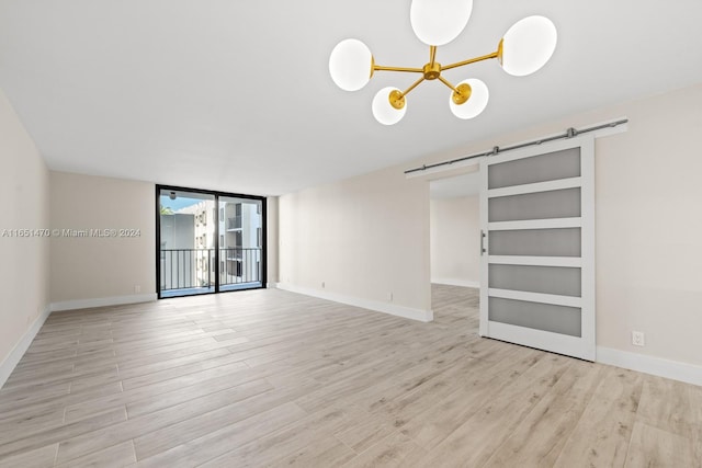 empty room featuring a notable chandelier, built in features, light hardwood / wood-style floors, and a barn door