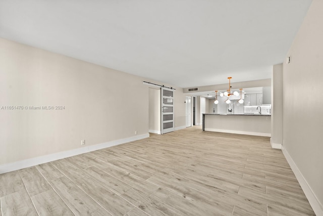 unfurnished living room with an inviting chandelier, light wood-type flooring, sink, and a barn door