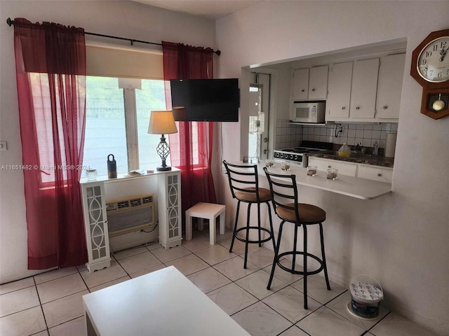 kitchen with white appliances, light tile patterned floors, kitchen peninsula, decorative backsplash, and white cabinetry