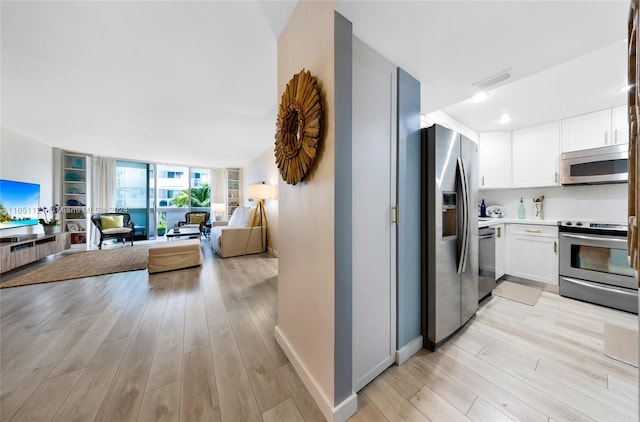 kitchen with light hardwood / wood-style flooring, floor to ceiling windows, appliances with stainless steel finishes, and white cabinetry