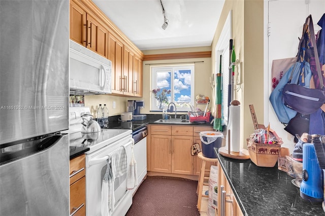 kitchen featuring sink, white appliances, rail lighting, and dark stone counters