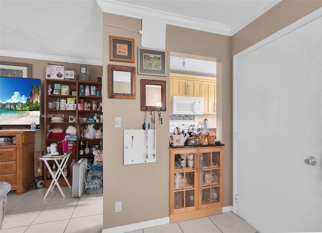 kitchen with light brown cabinets, light tile patterned flooring, a textured ceiling, and ornamental molding