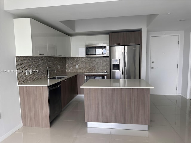 kitchen with light tile patterned floors, stainless steel appliances, sink, a kitchen island, and decorative backsplash