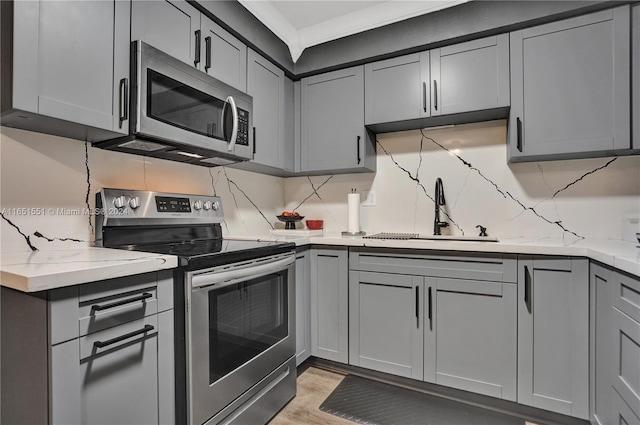 kitchen featuring stainless steel appliances, light stone counters, sink, decorative backsplash, and light hardwood / wood-style floors