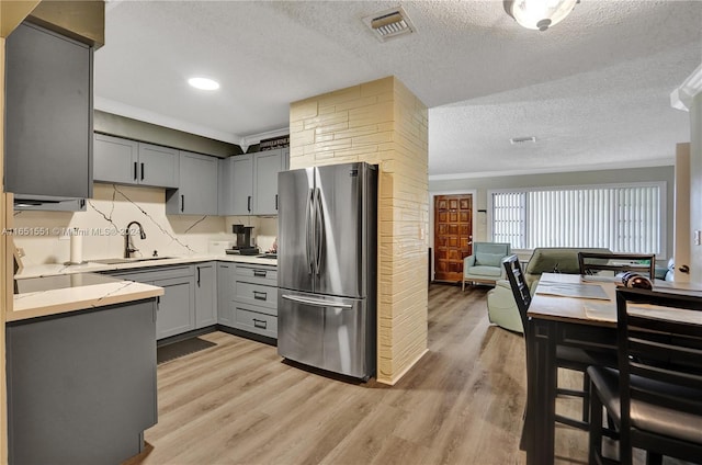 kitchen with a textured ceiling, gray cabinetry, stainless steel fridge, sink, and light wood-type flooring