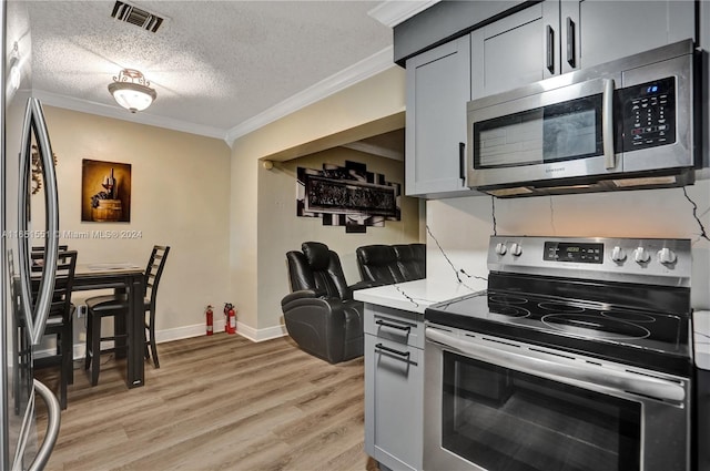 kitchen with ornamental molding, appliances with stainless steel finishes, a textured ceiling, and light hardwood / wood-style flooring