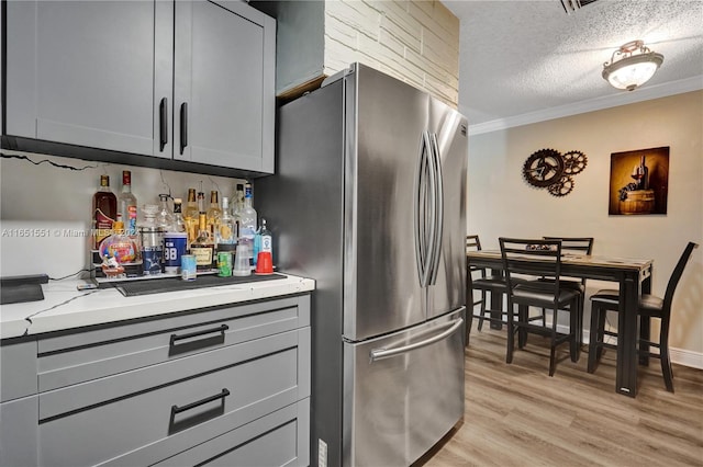 kitchen featuring a textured ceiling, gray cabinetry, light stone countertops, light hardwood / wood-style flooring, and stainless steel refrigerator