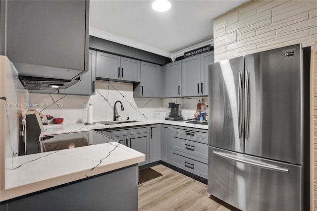 kitchen featuring light wood-type flooring, light stone countertops, stainless steel refrigerator, sink, and decorative backsplash