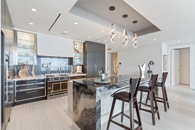 kitchen with a breakfast bar, dark stone countertops, hanging light fixtures, modern cabinets, and a raised ceiling