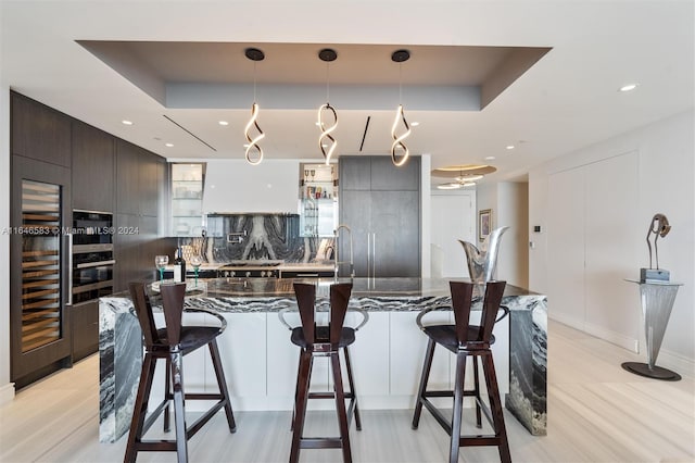 kitchen with decorative backsplash, a tray ceiling, modern cabinets, and a breakfast bar