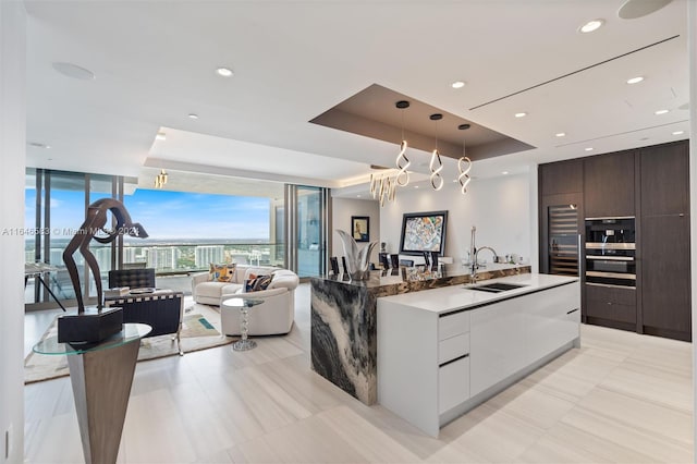 kitchen with a wall of windows, a raised ceiling, modern cabinets, and a spacious island