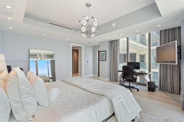 bedroom with recessed lighting, an inviting chandelier, light wood-type flooring, and a tray ceiling