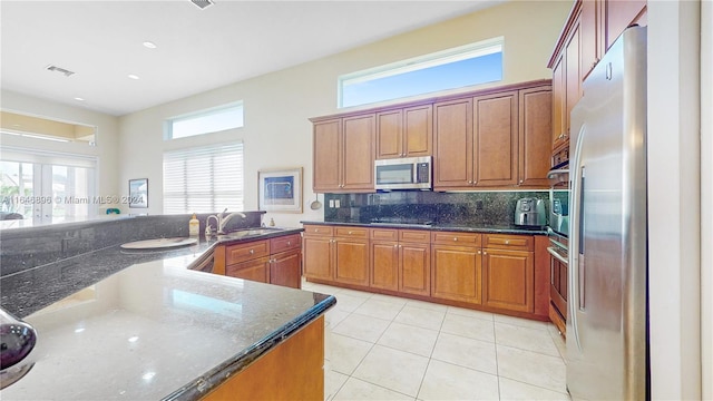 kitchen with dark stone counters, sink, decorative backsplash, appliances with stainless steel finishes, and light tile patterned flooring