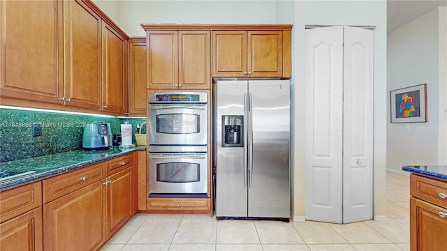 kitchen featuring appliances with stainless steel finishes, light tile patterned floors, and dark stone counters