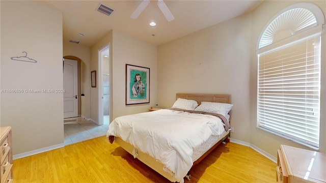 bedroom with ensuite bathroom, ceiling fan, light wood-type flooring, and multiple windows