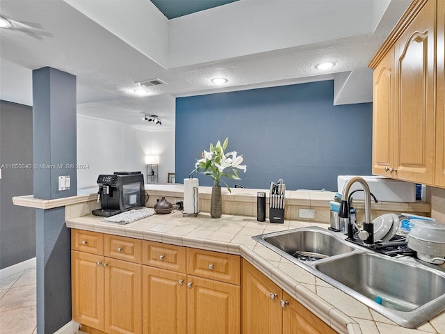 kitchen with kitchen peninsula, sink, light tile patterned floors, and tile countertops