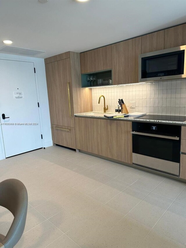 kitchen featuring backsplash, stainless steel appliances, sink, light stone countertops, and light tile patterned flooring