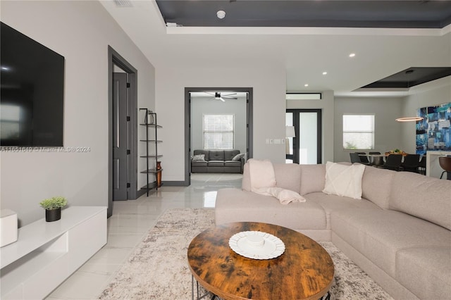 living room with a tray ceiling, a wealth of natural light, and ceiling fan