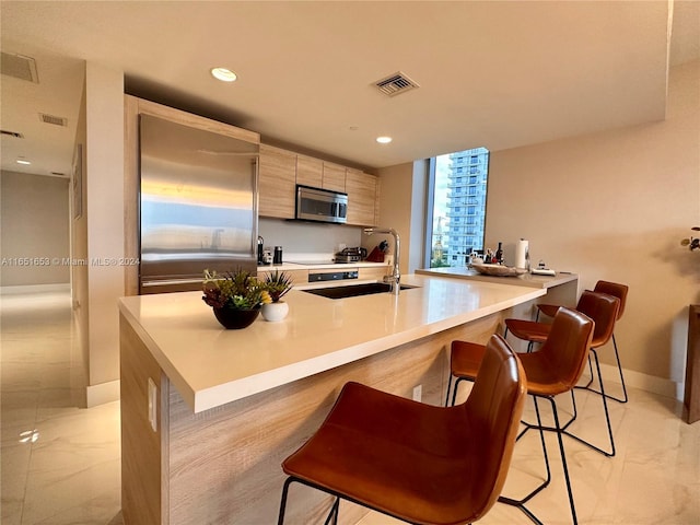 kitchen featuring light brown cabinetry, stainless steel appliances, sink, kitchen peninsula, and a kitchen breakfast bar