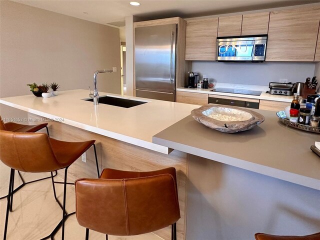 kitchen featuring light brown cabinets, a breakfast bar area, stainless steel appliances, and sink